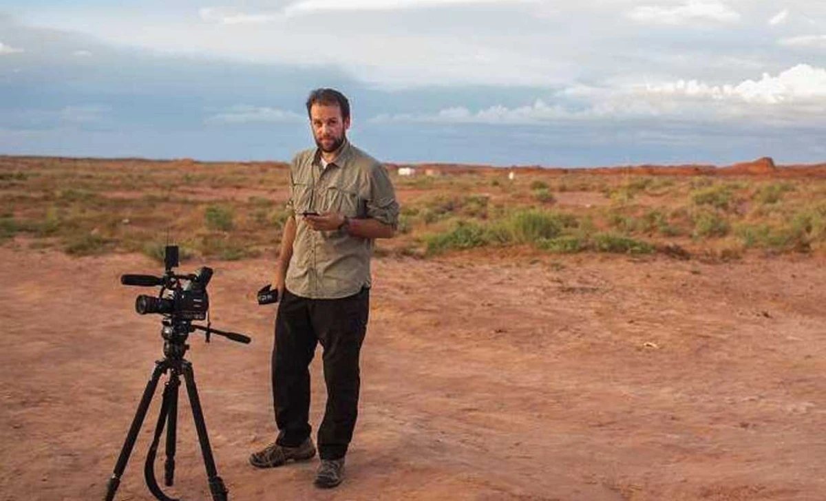 Matthew Mario Rivera standing outdoors with a camera on a tripod during a field production shoot
